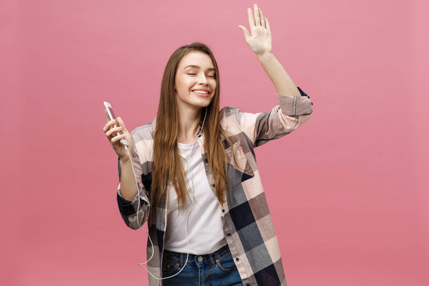 Lifestyle-Konzept. Junge Frau benutzt Handy zum Musikhören auf rosa Hintergrund - Foto, Bild