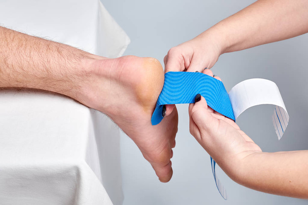 doctor physiotherapist hands applying kinesio medical taping on the ankle of a caucasian man. Closeup view - Zdjęcie, obraz