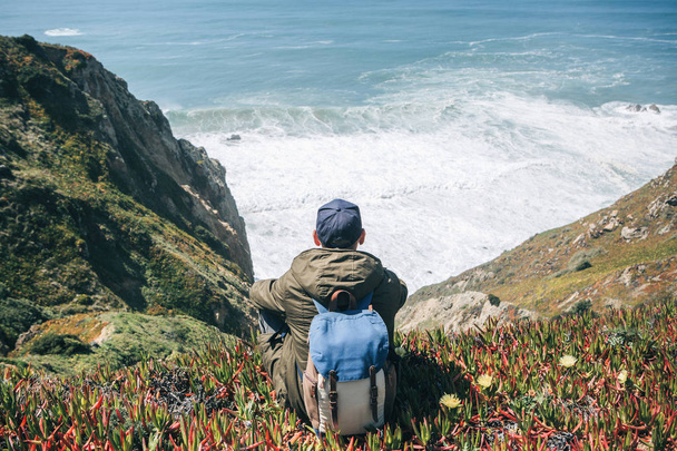 A tourist man with a backpack enjoys a beautiful view of the Atlantic Ocean on a spring day - Photo, Image