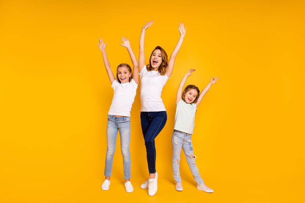 Full length body size portrait of three nice lovely slim attractive cheerful cheery positive ecstatic people having fun raising hands up isolated over bright vivid shine yellow background - Photo, image