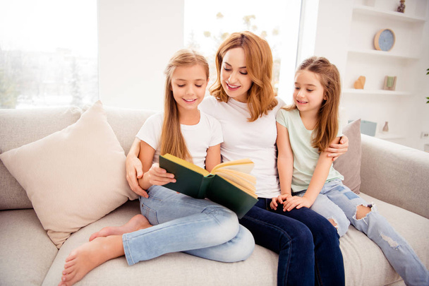 Portrait of nice cute adorable winsome lovely attractive charming cheerful cheery redhead people mom mommy mum reading book pre-teen girls sitting on divan in house indoors - Фото, изображение
