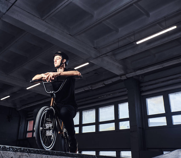 Подросток BMX сидит на велосипеде в скейтпарке в помещении
 - Фото, изображение