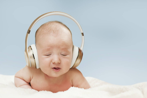 beautiful newborn baby in big headphones listening to music, isolated on blue background - Photo, Image