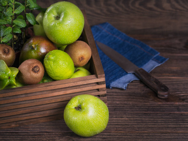 Healthy food background. Concept of healthy food. Fresh green fruits in box on dark wooden background. Set of green fruits for healthy diet and detox: apple, lime, kiwi, mango, carambola and mint. - Zdjęcie, obraz