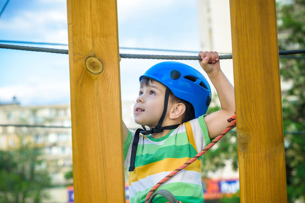 brave little boy having fun at adventure park and smiling to camera wearing helmet. toddler climbing in a rope playground structure. Scout practicing rappelling - Photo, image