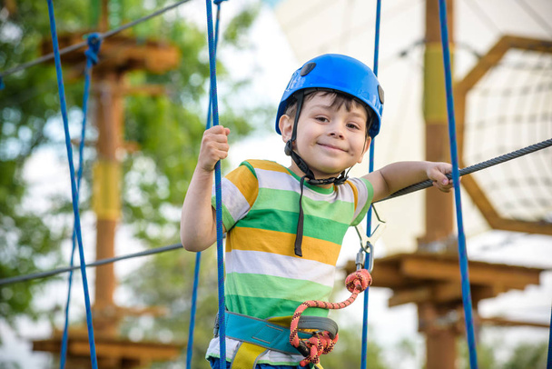 boy having fun at adventure park. toddler climbing in a rope playground structure. toddler climbing in a rope playground structure. Safe Climbing extreme sport with helmet and Carabiner - Foto, imagen