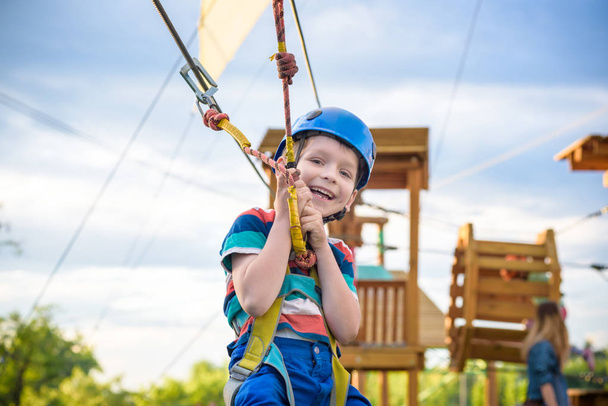 夏の晴れた日に登山の冒険公園での活動を楽しんでいる小さなかわいい男の子。クライミング ロープ遊び場構造での幼児。安全なクライミング ヘルメットとカラビナの極端なスポーツ。保険 - 写真・画像