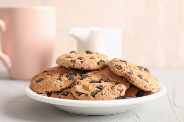 Piatto con gustosi biscotti al cioccolato e tazza sfocata di latte su sfondo grigio, primo piano
 - Foto, immagini