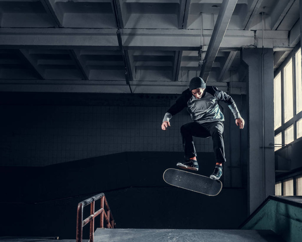 Молодой скейтбордист выполняет трюк на мини-рампе в скейт-парке в помещении
.  - Фото, изображение
