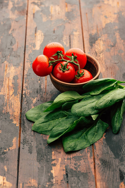 Verse spinazie en rijpe tomaten in een klei kom op een houten ondergrond, Groenen voor salade, vegetarisme, detox - Foto, afbeelding