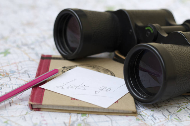 La inscripción en un pedazo de papel: "¡Vamos!". Los prismáticos y el cuaderno están en el mapa turístico
. - Foto, Imagen