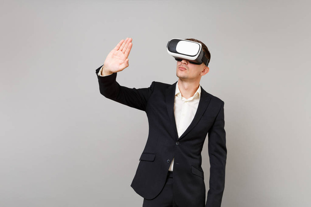 Young business man in suit looking in headset touch something like push click on button and pointing at floating virtual screen isolated on grey background. Achievement career wealth business concept - Photo, image