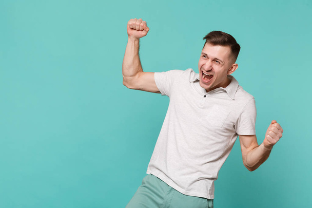 Portrait of happy young man in casual clothes expressive gesticulating with hands, screaming Yes isolated on blue turquoise background. People sincere emotions, lifestyle concept. Mock up copy space - Foto, Imagen