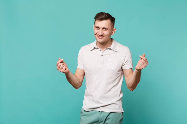 Smiling young man in casual clothes rubbing fingers, showing cash gesture, asking for money isolated on blue turquoise wall background. People sincere emotions, lifestyle concept. Mock up copy space - Photo, Image