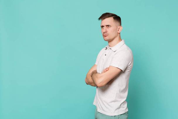 Portrait of concentrated young man in casual clothes looking aside holding hands folded isolated on blue turquoise background in studio. People sincere emotions, lifestyle concept. Mock up copy space - Photo, Image
