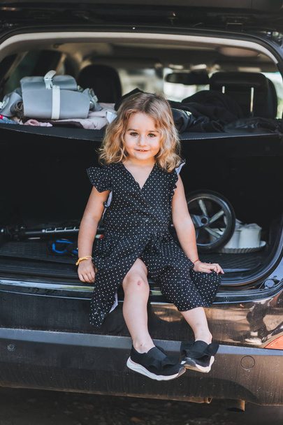 Uma menina pequena e bonita está sentada no carro
 - Foto, Imagem