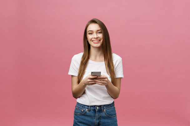 Photo of cheerful cute beautiful young woman chatting by mobile phone isolated over pink wall background. - Foto, Bild