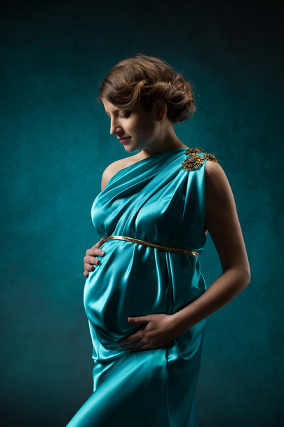 Pregnant woman in long silk dress over blue art background. - Photo, Image
