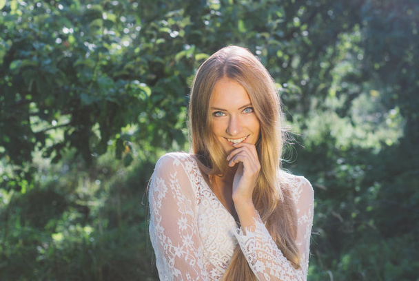 Retrato de niña sonriente hermosa en vestido de encaje blanco en el jardín de manzana, las manos cerca de la cara
 - Foto, Imagen