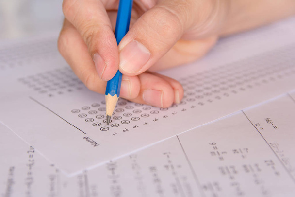 Studenten hand vasthouden potlood schrijven geselecteerde keuze op antwoordblaadjes en wiskunde vraagblaadjes. studenten die examen doen. schoolexamen  - Foto, afbeelding