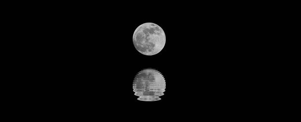 zilverkleurige grote volle maan met de reflectie op het zeewater om middernacht en de zwarte hemel - Foto, afbeelding