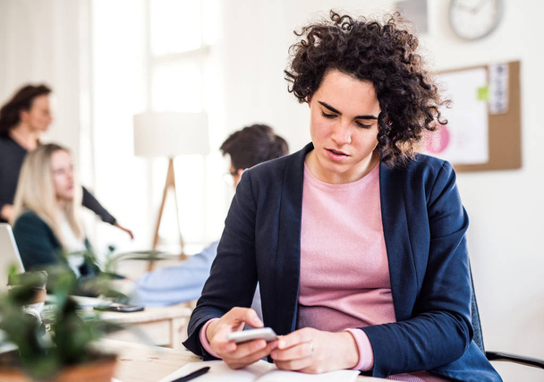 A portrait of young businesswoman with smartphone in a modern office. - Foto, afbeelding