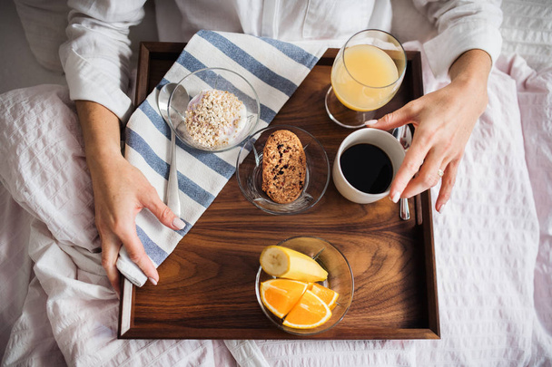 A midsection of woman with breakfast in bed in the morning. A top view. - Фото, изображение