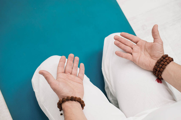 Concept of yoga and meditation. Close-up, hands of a man in white clothes, folded in prayer. White background and yellow-mini rubber mat. - Fotó, kép