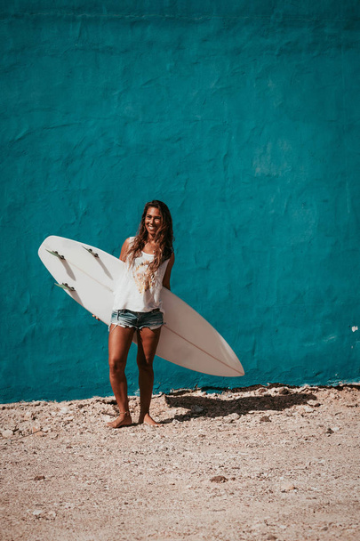 happy surfer girl with surfboard in front of blue wall - Foto, afbeelding