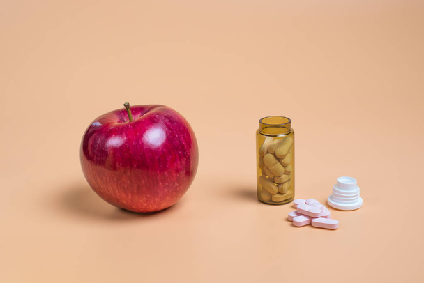 Pílulas cor-de-rosa na garrafa de vidro e maçã em um fundo laranja. Espaço de cópia para texto
 - Foto, Imagem