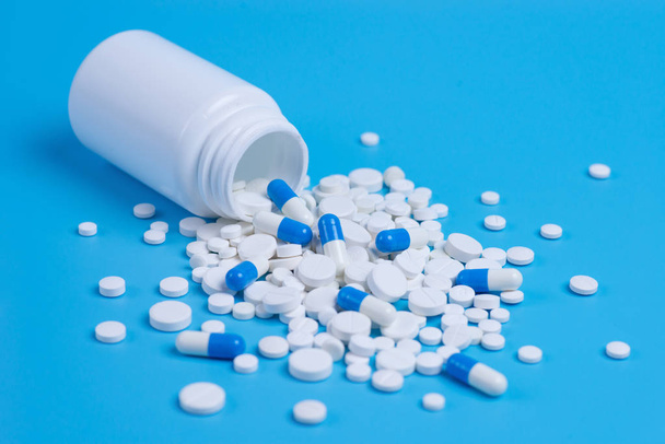 Wit en blauw pillen, tabletten en witte fles op blauwe achtergrond. Ruimte voor tekst kopiëren - Foto, afbeelding