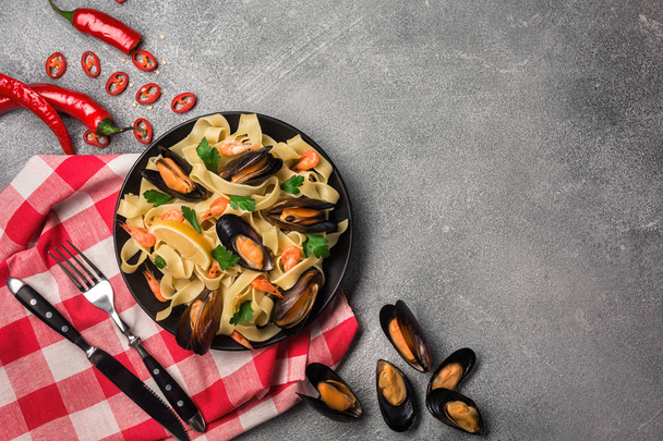 Domácí těstoviny špagety s mušlemi, chilli a petrželkou na kamenné pozadí. moře jídla. Pohled shora - Fotografie, Obrázek