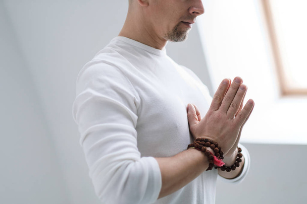 Мужчина в белой одежде на белом фоне со сложенными руками на груди. Медитация и молитва, йога
. - Фото, изображение