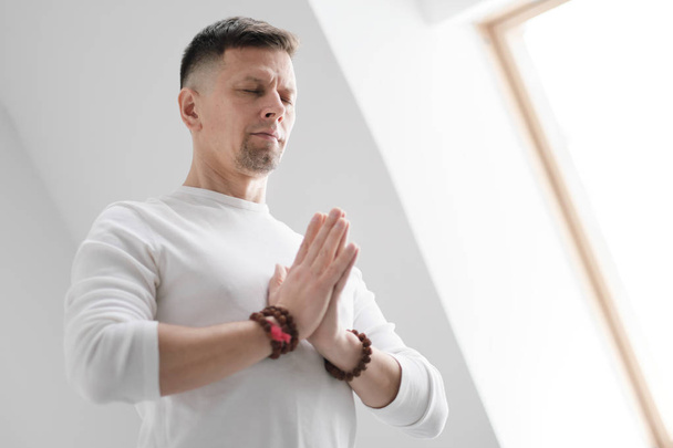 Чоловік у білому одязі на білому тлі зі складеними руками на грудях. Медитація і молитва, йога
. - Фото, зображення