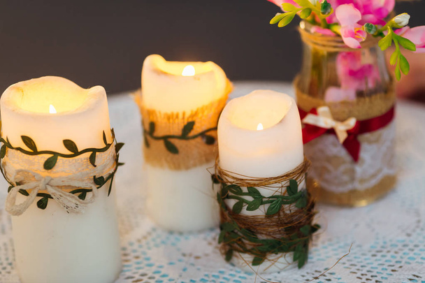 een close-up van kaarsen met een vuur en een transparante vaas met bloemen op een tafel met een tafelkleed - Foto, afbeelding