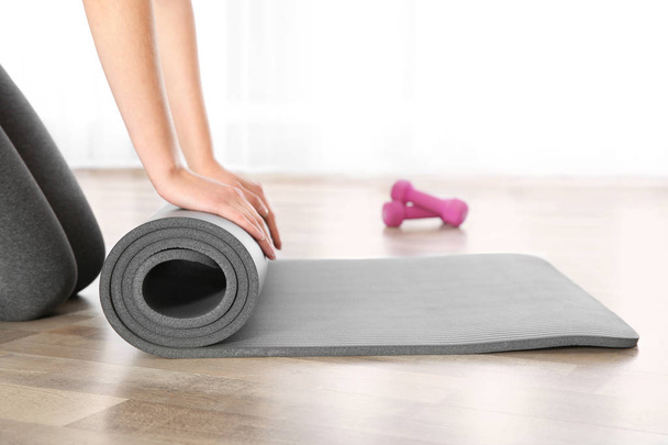 Woman rolling yoga mat on floor indoors, closeup - Foto, Imagem