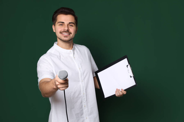 Young man in casual clothes holding microphone and clipboard on color background. Space for text - Foto, Imagem