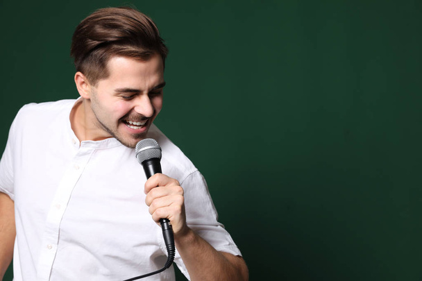 Young handsome man in casual clothes singing with microphone on color background. Space for text - Φωτογραφία, εικόνα