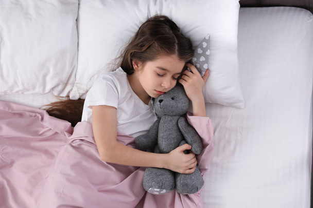 Beautiful little girl with toy rabbit sleeping in bed, top view - Foto, Imagem