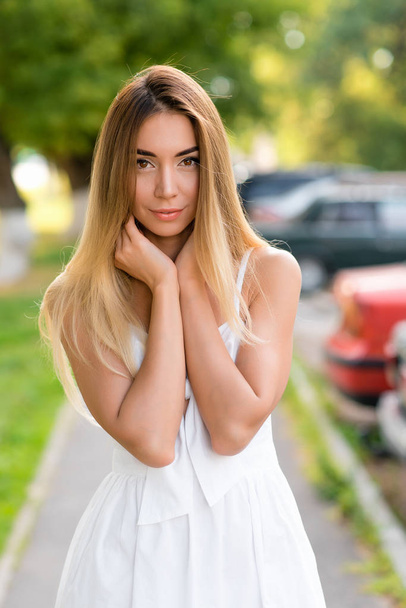Young and beautiful girl in park with long hair. Portrait of a woman in summer outdoors. Tanned skin and casual makeup. Emotionally tender smile and insightful look. Happy smiling resting. - 写真・画像