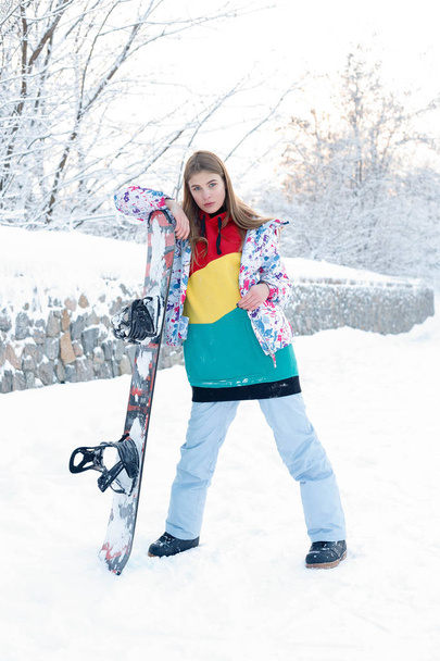 woman winter outdoor snowboarding concept. Young woman holding snowboard on her shoulders, she's looking away and smiling, copy space, close up - Фото, изображение