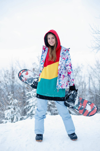 woman winter outdoor snowboarding concept. Young woman holding snowboard on her shoulders, she's looking away and smiling, copy space, close up - Фото, изображение