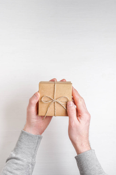 man's hands holds a gift in a box on a white wooden background - Фото, изображение