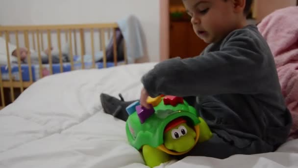 Criança em pijama brincando com brinquedo de educação de tartaruga no mau com bebê recém-nascido no berço por trás do conceito de desenvolvimento inicial
 - Filmagem, Vídeo
