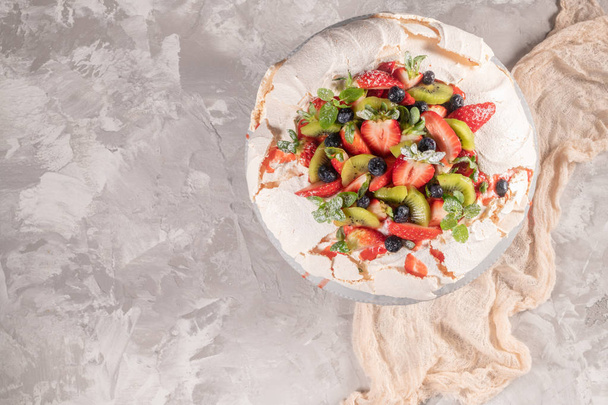 Vintage cake stand with Meringue dessert Pavlova with sugar powder, fresh strawberries, kiwi, blueberries and mint. Homemade baking. Copy space. Top view. Flat lay - Photo, image