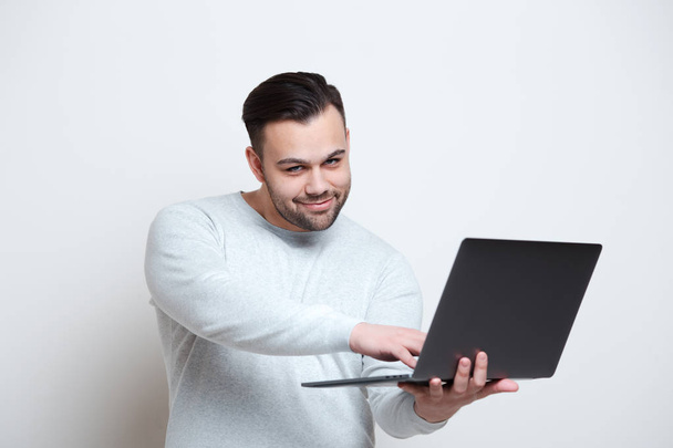 Porträt eines jungen Mannes, der auf Laptop-Tastatur vor weißem Hintergrund tippt - Foto, Bild