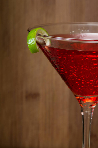 Close up of a Cosmo served in a martini glass garnished with a lime over a wooden background - Photo, Image