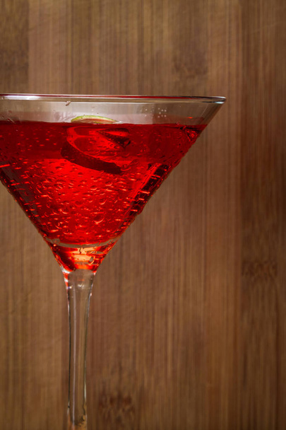 Gros plan d'un Cosmo servi dans un verre à martini garni d'une lime sur un fond en bois
 - Photo, image
