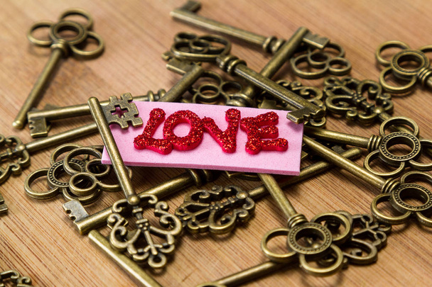 imagen conceptual utilizando teclas antiguas con una etiqueta rosa con letras de purpurina roja deletreando la palabra amor sobre un fondo de madera
 - Foto, Imagen