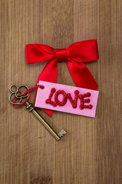 conceptual image using a red bow, an old key with a pink tag with red glitter letters spelling the word love - Photo, image